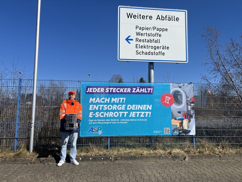 Abfallberater Jan Grunau posiert vor dem Kampagnenposter der Initiative "Jeder Stecker zählt"