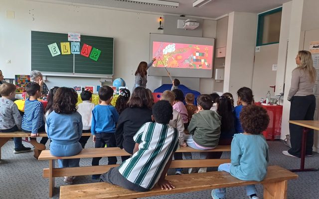 Kinder sitzen auf Bänken und sind von hinten zu sehen.