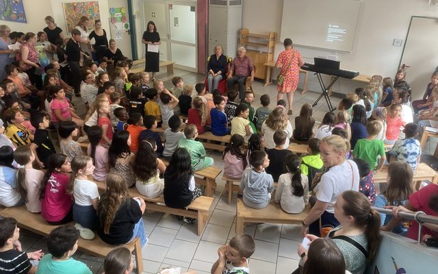 Kinder sitzen auf Bänken mit Blick auf Frau Amedick und ihren Mann.