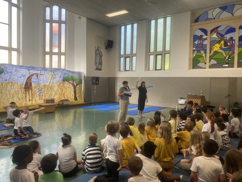 Alle Kinder sitzen zusammen in der Aula, Frau Haake hält den Pokal hoch.