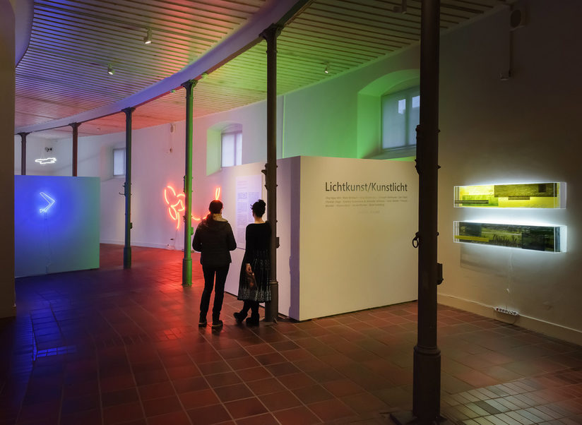 Ausstellungsansicht vorm Eingang zu Lichtkunst/Kunstlicht mit zwei Besuchenden.