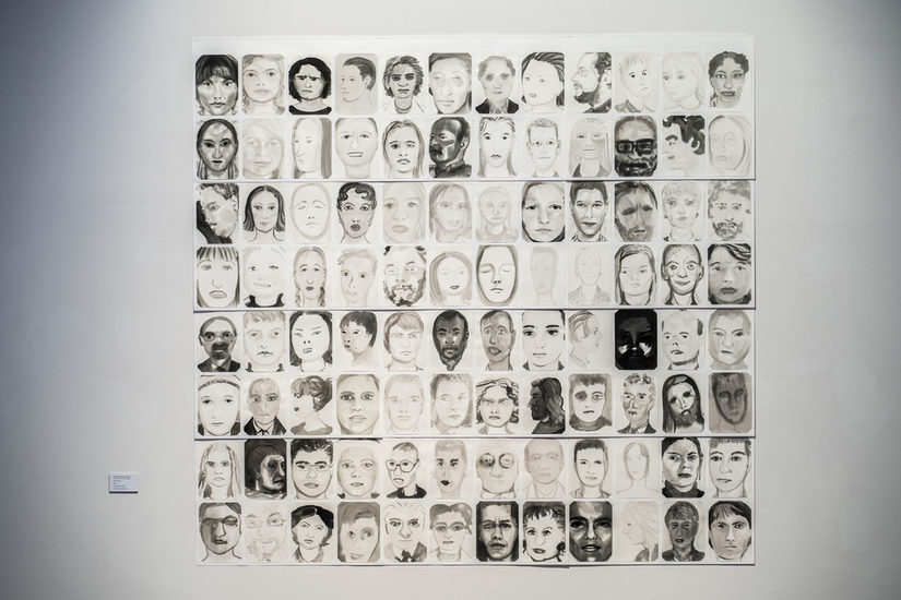 Fotografie einer Collage von vielen schwarzweißen Portraits in quadratischer Anordnung auf weißer Wand.