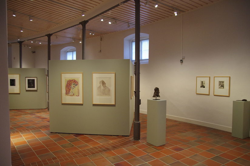 Innenaufnahme des Kunstmuseums mit gerahmten Bildern an weißen Stellwänden und kleinen Skulpturen auf Podesten.