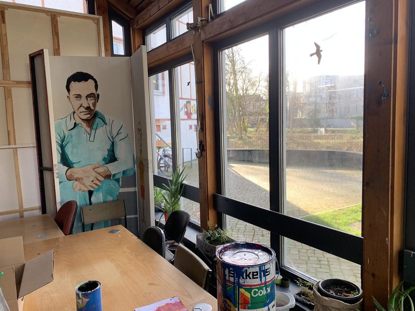 Auf dem Foto ist ein Ausschnitt des Ateliers zu sehen. Rechts ist eine Fensterfront mit Blick auf den Innenhof. Rechts stehen Tische, auf denen unterschiedliche Farbtöpfe stehen.