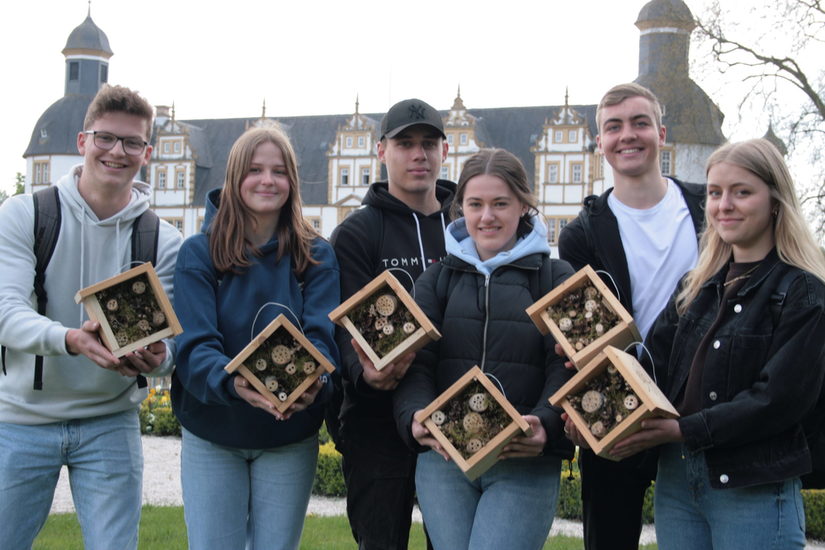 Foto einer Gruppe von sechs weißen Jugendlichen vor dem Schloss Neuhaus mit quadratischen Nisthilfen aus Holz in den Händen.