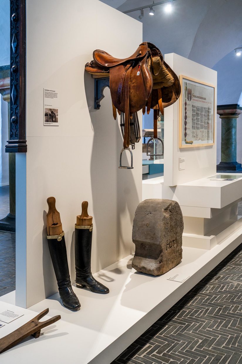Ausstellungseinheit, die Hussarenstiefel und Sattel mit weiteren Informationen zeigt.