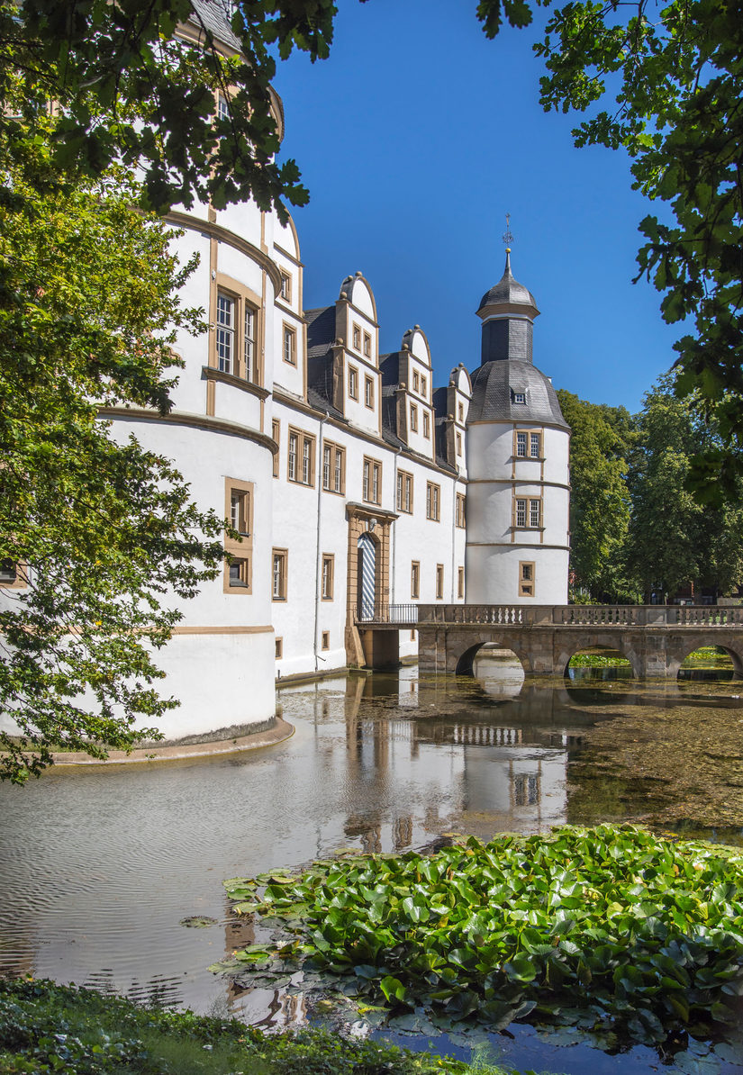 Frontseite von Schloss Neuhaus, seitlich fotografiert mit umgebendem Wassergraben und Brücke zum Eingangstor bei Tageslicht.