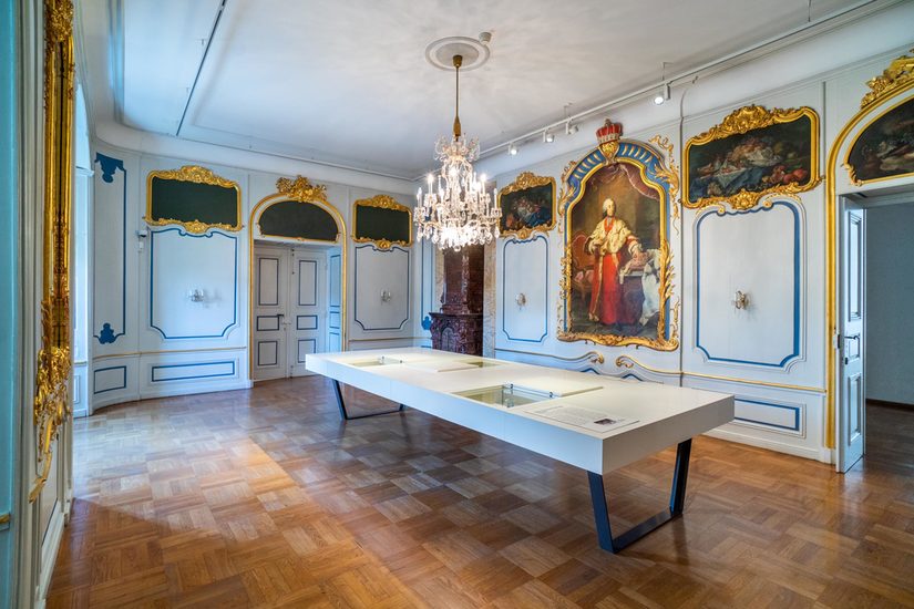 Innenaufnahme des Speisezimmers mit weißem Tisch in der Mitte des Raums, auf dem Informationen und Objekte ausgestellt sind.