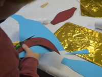 Eine Kinderhand schneidet den Flügel eines Engels aus bunter Pappe aus