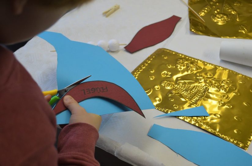 Eine Kinderhand schneidet den Flügel eines Engels aus bunter Pappe aus