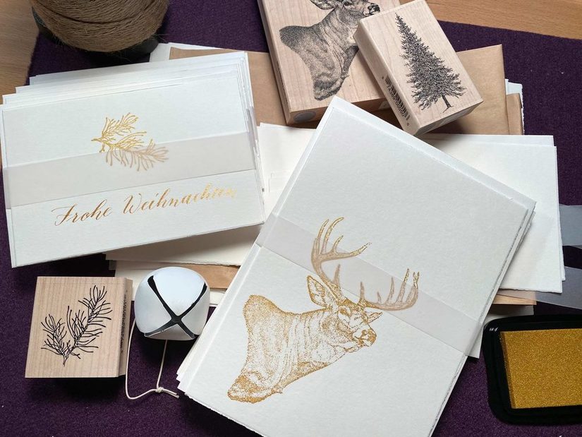 Es sind verschiedene Karten zu sehen auf denen mit Kalligraphie gezeichnet wurde. Unter anderem ein Hirsch oder ein Weihnachtsbaum in Gold