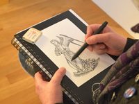 Ein Mensch hält einen Zeichenblock in der Hand und zeichnet mit Bleistift einen Engel