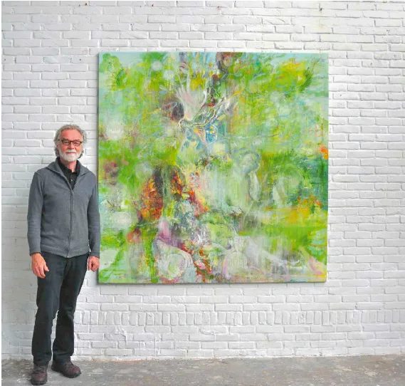 Ganzkörperfoto von Uwe Poth links neben einem seiner bunten, abstrakten Großformate vor einer weißen Wand.